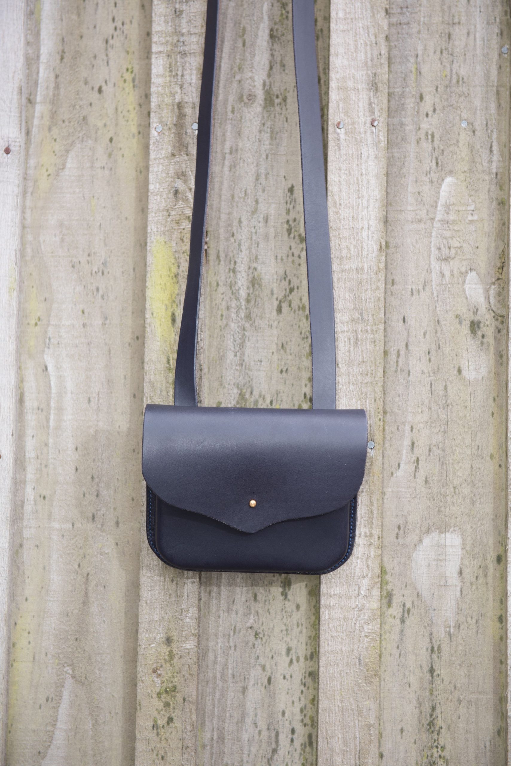 Small moulded navy blue handbag hanging against wooden door